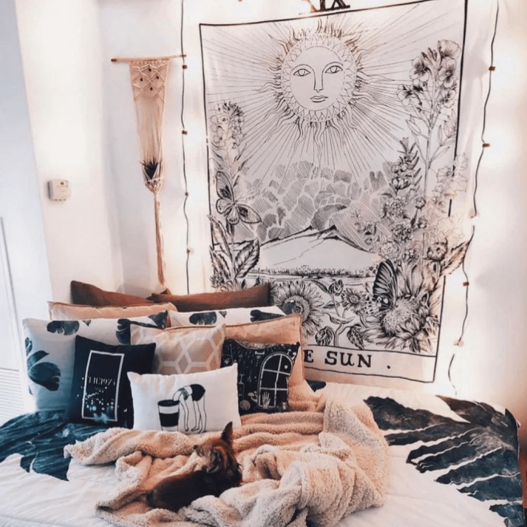 Bed made with pillows and The Sun tapestry hung on the wall with string lights