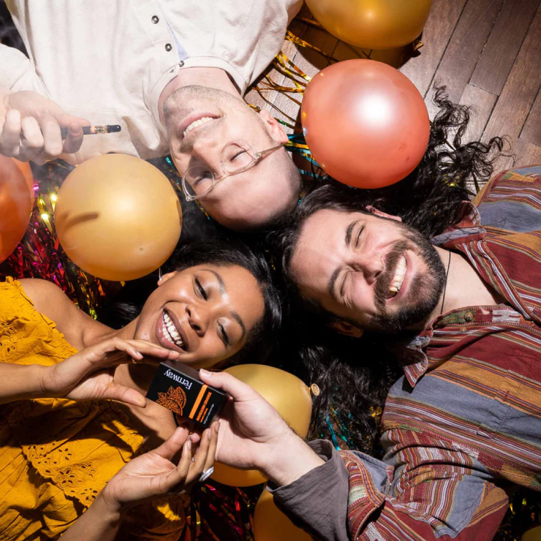 Group of friends smiling holding Fernway products laying down on a party floor