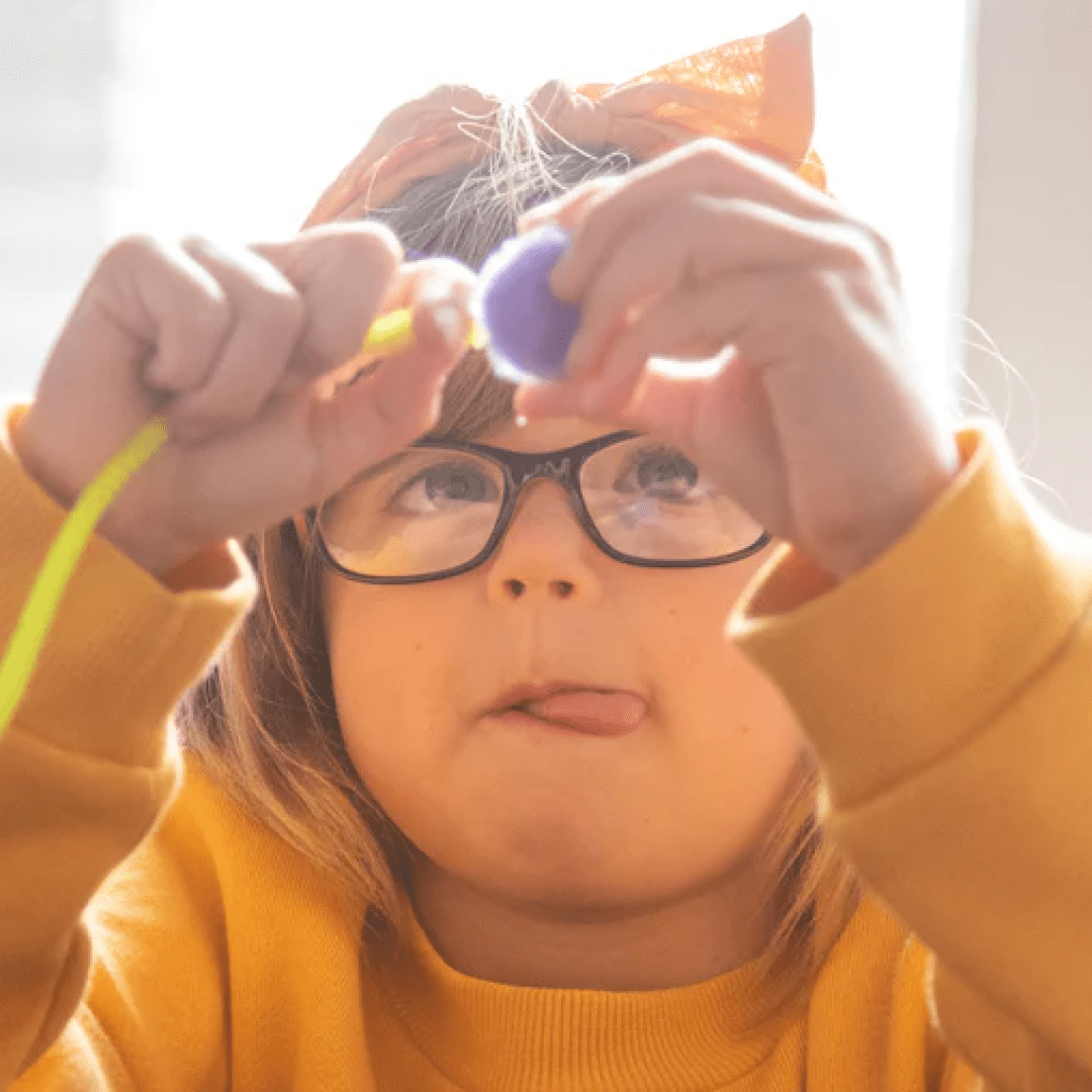 Little girl with glasses sticking her tongue out as she focuses and plays